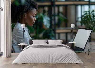 Close-up shot of an African American businesswoman working on a laptop with a blank screen on her desk in a modern office setting. Wall mural