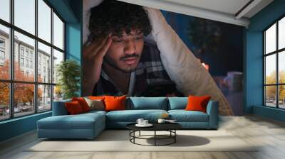 Gadget internet social media addict guy Latino tired man Arabian confused worried puzzled Indian male at night evening dark home under blanket cover with duvet scrolling mobile phone upset frustrated Wall mural