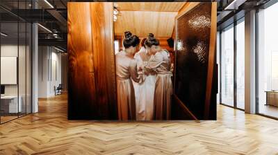 Girlfriends of the bride help to dress the bride in the hotel room. Wall mural