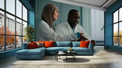 Medical people two professional doctors colleagues arabian young woman therapist discuss electronic health test results with african senior man use computer application doing online digital diagnostic Wall mural