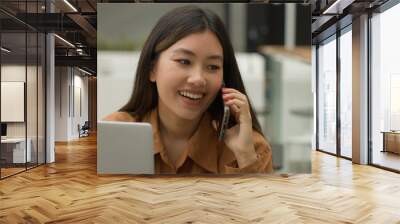 Smiling Asian woman businesswoman working online with laptop in office chinese japanese girl student freelancer talk mobile phone laughing excited female answer smartphone call carefree conversation Wall mural