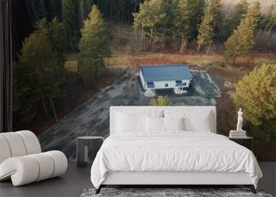 Aerial view of unfinished home with a blue roof and a modern white facade. Two entrances. Unfinished construction and unfinished yard near the house. White building on the background of a pine forest Wall mural