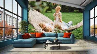 mother with children having fun in a hammock. Mom and kids in a hammock. The family spends time with the children in the garden. Wall mural