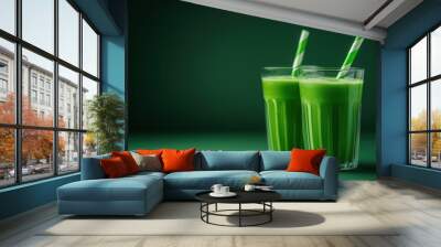 Two transparent glasses with straws with green smoothie on green background. Pair of glasses with thick green drink against empty space. Wall mural