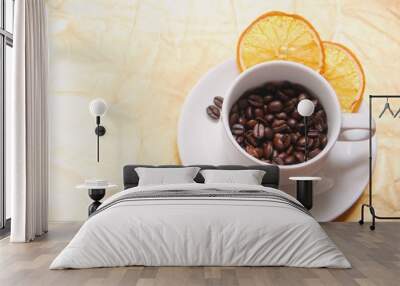 Cup and saucer filled with roasted coffee beans, with two slices of dried orange and two of coffee beans. Cup and saucer, coffee beans, slices of dried orange on a gold background. A white cup and Wall mural