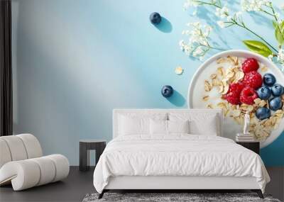 A bowl of yogurt with granola, blueberries, and raspberries on a light blue background with white flowers. Wall mural