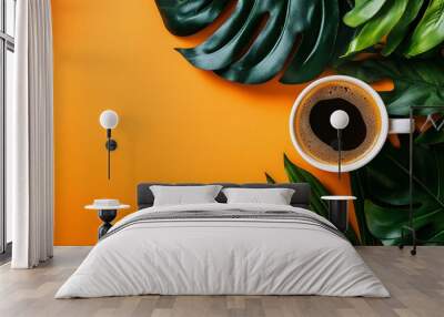 A cup of coffee on an orange background with tropical leaves around it. Wall mural