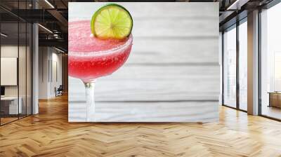 A single glass of pink cocktail with a lime wedge garnish sits on a white wooden surface. Wall mural