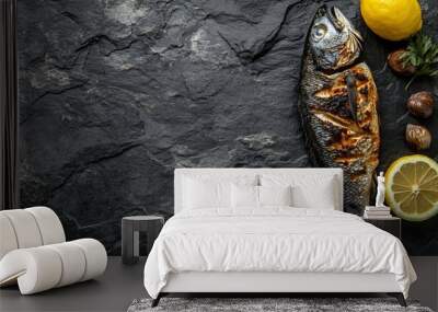 Grilled fish on a black slate background with lemon and garlic. Wall mural