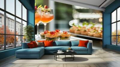 Two glasses of orange cocktails with ice and garnished with green leaves and pink flowers and mini desserts with orange jelly and red berries. Wall mural