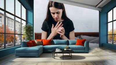 Close up of sad tired woman suffering from pain in hand or wrist sitting on bed at home, girl patient touching wrist feeling hurt joint pain having osteoarthritis disease health problem Wall mural