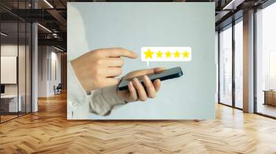 A woman is holding a cell phone and pointing to a five star rating Wall mural