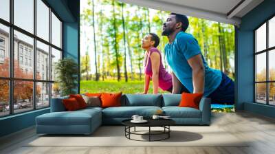 An attractive young woman and man doing yoga in green forest Wall mural