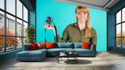 blonde woman holds a small camera in studio on blue background Wall mural