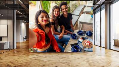 fashionable indian friends couple of two woman and man making selfie mobile phone.friends long-awaited meeting students eating pancake drinking masala tea after shopping.summer instahram lifestyle Wall mural