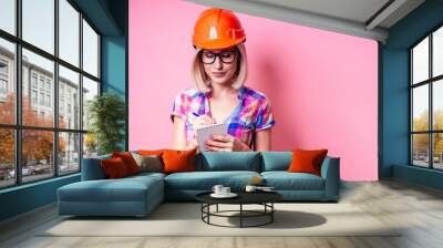 Female painter using roller for refurbishing color of pink wall indoors.smiling woman in business checkered shirt wearing builder helmet painting the walls in the apartment Wall mural