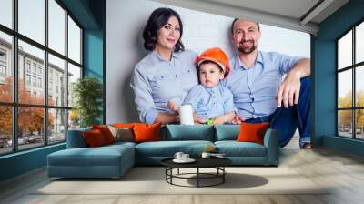 happy family handsome man in helmet hardhat and charming woman and their cute little son sitting on the floor against a white wall . concept of repairs house ( apartment ) by young family Wall mural