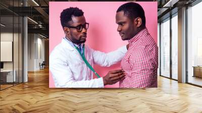 happy male african medical surgeon cardiologist doctor in a white coat and patient on a pink background in the studio. Wall mural