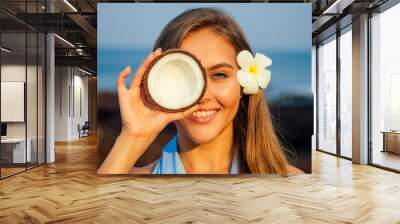 Portrait of beautiful girl close-up snow-white smile,blue eyes and perfectly clean skin holding an open dry coconut near face.female model on the beach happy tropical paradise coco nut oil face care Wall mural