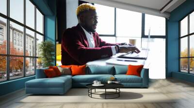 Smiling businessman in a marsala jacket working on laptop computer in office Wall mural