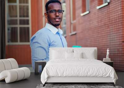 stylish and young African student American man holding glass with coffee in summer in park red brick building background Wall mural