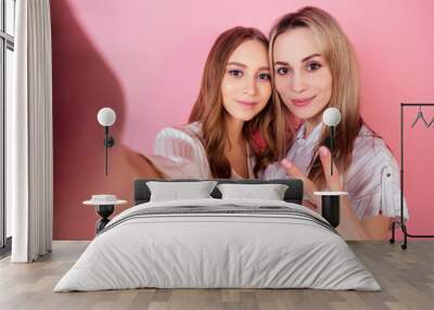 two beautiful and smiling female persons (mother and daughter) take photos selfie on the phone on a pink background in the studio. concept of love and family Wall mural