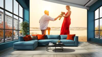 wife and husband happy couple on vacation by the sea.beautiful woman in red dress with a ring on her finger and loving man in a white shirt with a bouquet of roses romantic sunset.Valentine's day date Wall mural