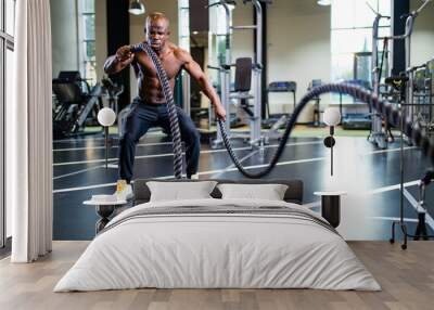 young african muscular athlete working out with ropes in gym Wall mural