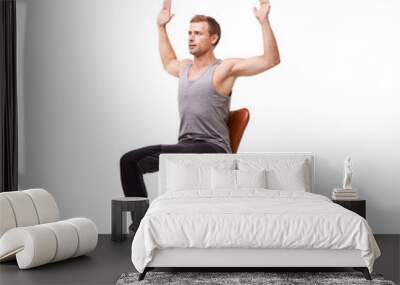 Stretching out his chest. A handsome young man wearing gym clothes and stretching while seated in an office chair against a white background. Wall mural