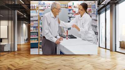 Assuring clients are informed. Shot of a young pharmacist helping an elderly customer at the prescription counter. Wall mural