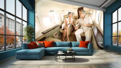 First-class all the way. Smiling and happy couple seated in a private jet and toasting each other while heading on a trip. Wall mural