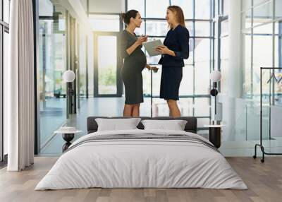 Sharing ideas in the office. Shot of two businesswomen talking together over a digital tablet in a modern office. Wall mural