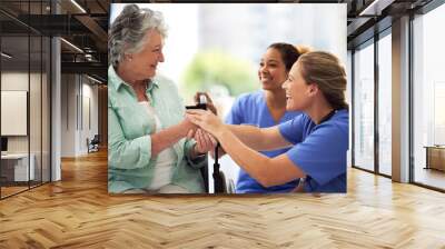 Shot of a smiling female doctor and nurse talking with a senior woman in a wheelchair Wall mural