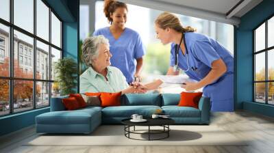 Shot of an attractive female nurse holding medical records while shaking hands with her wheelchair-bound senior patient in the hospital Wall mural