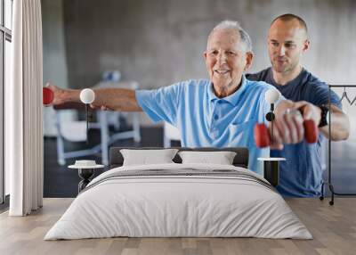 You're getting stronger every day. Shot of a physiotherapist helping a senior man with weights. Wall mural