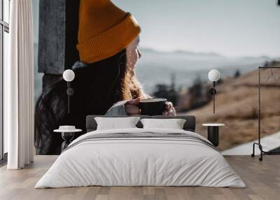 Woman with cup of coffee is sitting in front of mountain view and look away Wall mural