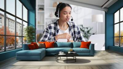 A young African American businesswoman in a headset communicates using video call. Ethnic female student talking while looking at laptop computer, online office conference, virtual learning concept. Wall mural