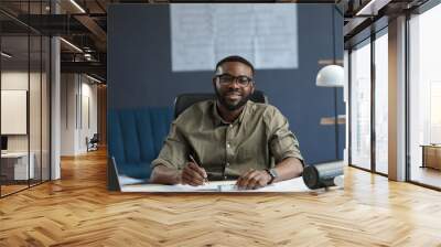 Afro-American architect working in office with laptop.Business portrait of black handsome bearded man wearing eyeglasses sitting at workplace.Confident businessman became successful.Business concept. Wall mural