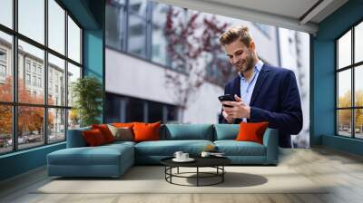 Handsome businessman using smartphone and smiling. Happy young man using mobile phone apps, texting message, browsing internet, looking at smartphone. Young people working with mobile devices. Wall mural