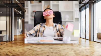 The concept of a lot of work. Tired Indian student girl sleeping with stickers on her eyes while sitting at the table. Distracted woman in home office. Wall mural