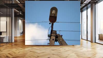 Old concrete lighting pole with a single lamp and wires against the sky with fluffy white cloud. View from the bottom.  Wall mural