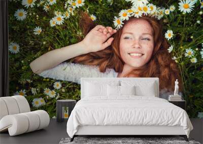 beautiful young girl with curly red hair in camomile field Wall mural