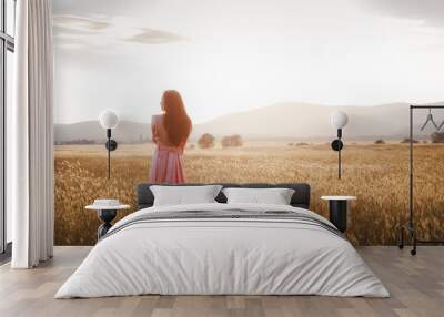 girl dancing in a field in a beautiful pink dress at sunset Wall mural