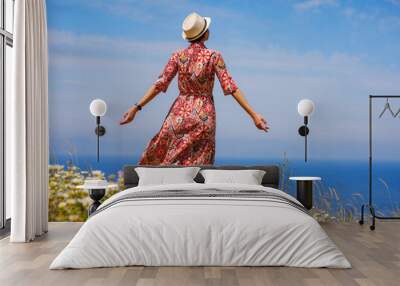 summer trip to Rhodes island, Greece. Young Asian woman in ethnic red dress walk to viewpoint over city of Rhode in daisy flowers. Tourism, vacation, solo travel and discovery concept Wall mural