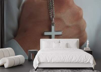 Closeup shot of a religious male holding a silver necklace with a cross pendant Wall mural