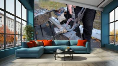 At the smithy workshop. Blacksmith’s hands holding forceps and a hammer forging a metal billet, horseshoe, on an anvil Wall mural