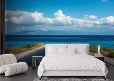 Tranquil asphalt road to ocean on summer beach, ideal for tourism trips, under blue sky, shore view Wall mural