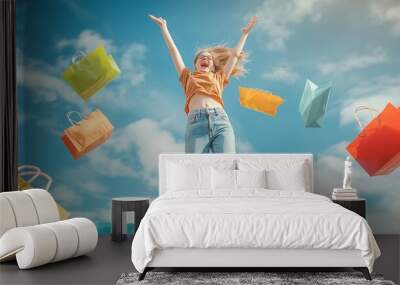 A young woman in casual attire is seen jumping with joy amidst a flurry of colorful shopping bags against a backdrop of a clear blue sky, symbolizing excitement and freedom in shopping. Wall mural