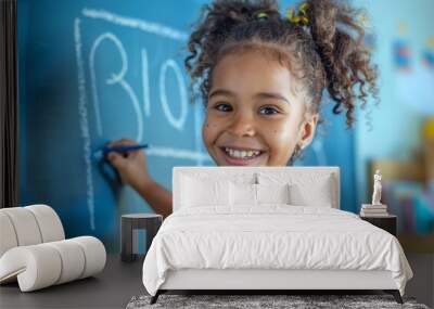 In a classroom, a cheerful young girl in a bright yellow outfit happily draws on a chalkboard. Her artistic activity boosts intelligence and supports growth, promoting a positive learning environment Wall mural