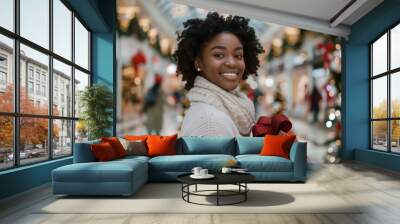 In a festively decorated shopping mall, a young woman exudes joy while shopping for Christmas gifts, her bright smile adding to the holiday spirit and her stylish embrace of the season Wall mural